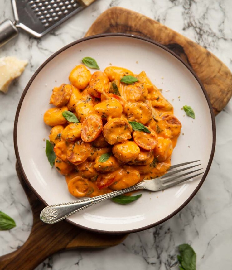 overhead shot of creamy chorizo gnocchi on small white plate with silver fork on wooden chopping board