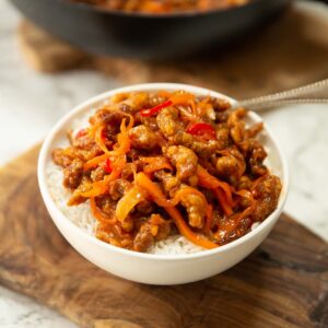 crispy chilli beef served over rice in small white bowl on chopping board