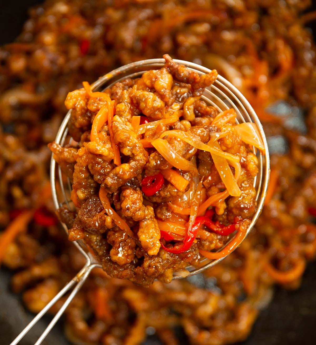close up overhead shot of slotted spoon lifting crispy chilli beef out of pan