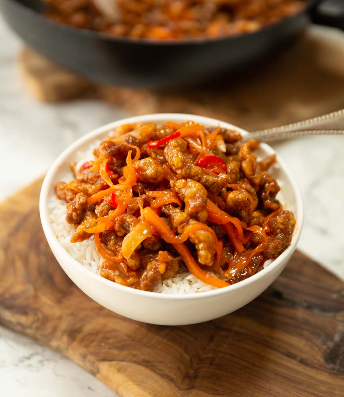 crispy chilli beef served over rice in small white bowl on chopping board
